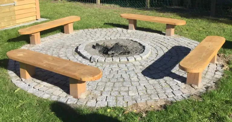 Fire plankebænke i massivt træ sat rundt om en brolagt bålplads på græsplænen.