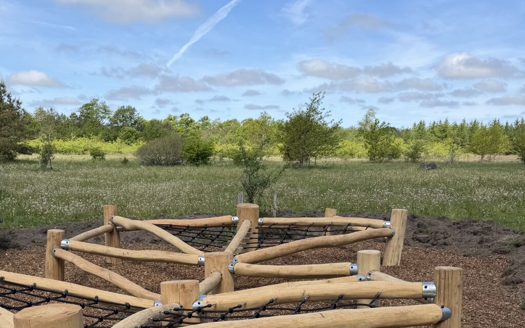 Naturlegeplads i robinie med klatrenet i Aaby Skoven, omgivet af eng og skov under blå himmel