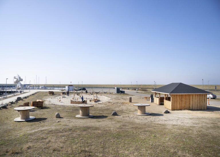 Langhuset og kabeltromlerne ved aktivitetsområdet på Esbjerg Strand, med legeområdet bagved