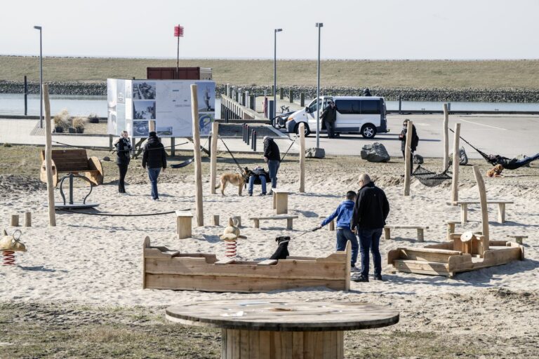 Familier med børn i sandlegeområdet ved Esbjerg Strand med legebåde i træ og stolper i sandet